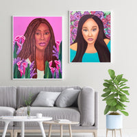 Framed prints in a living room with a grey couch and plant. Wall art prints of 2 African American women with purple flowers. 